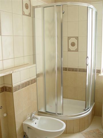 Jasna łazienka z kabiną prysznicową narożną z przesuwnymi drzwiami i bidetem, wykończona beżowymi płytkami z dekoracyjnymi wstawkami.